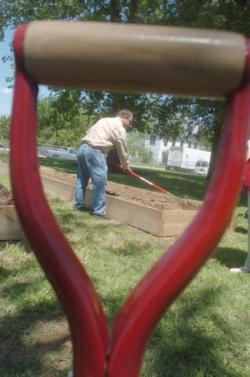 A man working in a raised bed as seen through a spade handle